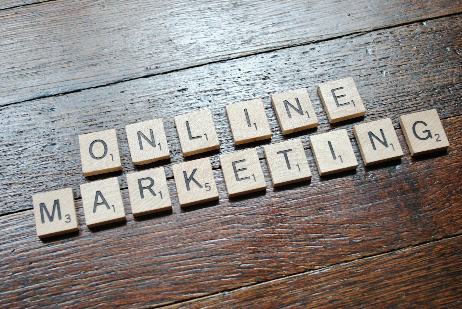Scrabble tiles arranged to spell 'ONLINE MARKETING' on a wooden table with a textured surface.